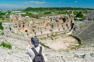 ein männlich Tourist genießt ein gehen durch das Amphitheater unter das Ruinen von das uralt Stadt von perge, im Truthahn. das Tourist sieht aus um das uralt Stadt von perg mit Faszination und nimmt Fotografien foto