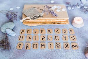 skandinavisch Runen zum Vermögen erzählen sind im drei Reihen, ein Buch, Steine und ein Kerze auf das Tabelle foto