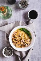 asiatisch Suppe mit Reis Nudeln, Pilze und Grün Zwiebeln im ein Schüssel oben und Vertikale Aussicht foto