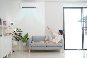 jung Mann genießen Komfort mit Fernbedienung Steuerung zum Luft Konditionierung beim Zuhause foto