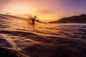 Dezember 14, 2022. Bali, Indonesien. Mann im Ozean während Surfen mit Sonnenuntergang oder Sonnenaufgang Töne. Surfer Reiten auf Welle und machen Tricks. foto