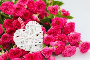 dekorativ Weiß Herz gemacht von Reben, Valentinstag Tag auf das Hintergrund von ein Strauß von Rosen. foto