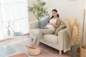 glücklich schwanger Frau mit Kopfhörer Hören zu Mozart Musik- und Lügen auf Sofa, Schwangerschaft Konzept foto