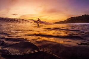 Dezember 14, 2022. Bali, Indonesien. Mann im Ozean während Surfen mit Sonnenuntergang oder Sonnenaufgang Töne. Surfer Reiten auf Surfbrett im Welle. foto