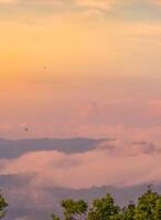 das atemberaubend Aussicht von ein Touristen Standpunkt wie Sie gehen Nieder ein Hügel auf ein nebelig Weg mit ein Hügel und ein Hintergrund von ein golden Himmel im Wald Park, Thailand. Regenwald. Vogel Auge Sicht. Antenne Sicht. foto