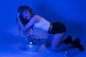 Sinnlichkeit Frau mit Spiegel Disko Ball posieren kniend im Blau Neon- farbig Beleuchtung im Nachtclub foto