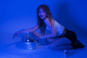 Frau sinnlich halten Spiegel Disko Ball, kniend im Blau Neon- farbig Beleuchtung Nacht Verein Party foto