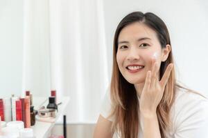 schön asiatisch Frau Lächeln verwenden Sahne zum gut Haut. Gesicht von ein gesund Frau anwenden Sahne und bilden. Werbung zum Haut Creme, Anti-Falten, Baby Gesicht, bleichen, Feuchtigkeitscreme, spannen Poren Serum foto