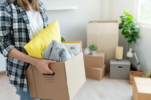 ziehen um Haus, Verlegung. Frau halt Karton Box enthalten Ausrüstung zum Neu Eigentumswohnung, Innerhalb das Zimmer war ein Karton Box enthält persönlich Besitz und Möbel. Bewegung im das Wohnung foto