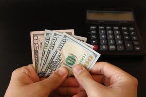 Mann Zählen uns Dollar Geld mit seine Hand. uns Banknoten. das Papier Währung von USA .Taschenrechner im das Hintergrund. foto