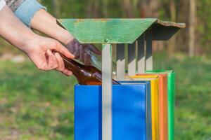 Hand werfen Glas Flasche im vier Farben Recycling Behälter im das Park foto