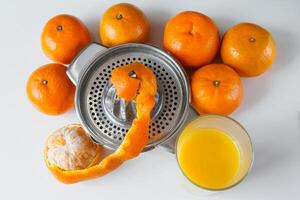 Handbuch Metall Entsafter umgeben durch Mandarinen und ein Glas von Saft auf Weiß Hintergrund foto