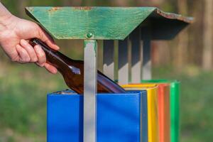 Hand werfen Glas Flasche im vier Farben Recycling Behälter im das Park foto