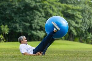 Senior asiatisch Mann ist ausüben im das Öffentlichkeit Park mit Yoga Ball zum Ader Körper und Abdomen Muskel Gebäude zum stark ältere Gesundheitswesen foto