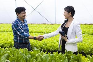 Händeschütteln zwischen asiatisch Farmer und seine Neu lokal Geschäft Unternehmer Innerhalb seine Hydrokultur Salat Grüner Salat Gewächshaus zum Neu Partnerschaft foto