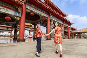 Rückseite Aussicht von asiatisch Frau und ihr Senior Mutter im rot cheongsam Qipao Kleid ist Besuch das Chinesisch Buddhist Tempel zusammen während Mond- Neu Jahr zum traditionell Kultur Konzept foto