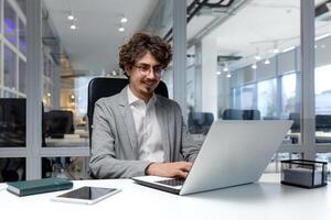 heiter und erfolgreich Geschäftsmann Innerhalb Büro Arbeiten mit Laptop, bärtig Mann lächelnd und Tippen auf Laptop Klaviatur, Programmierer Codierung Software im modern Zimmer. foto