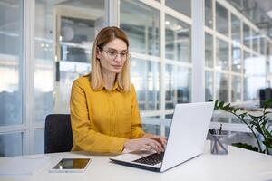 konzentriert reifen Frau im ein hell Büro Rahmen Arbeiten aufmerksam auf ihr Laptop zum Geschäft Zwecke. foto