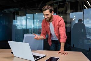 Wirksam und erfolgreich Geschäftsmann reden auf Anruf mit Kollegen, online treffen. ein Mitarbeiter funktioniert Innerhalb ein modern Büro, Verwendet ein Laptop beim arbeiten. foto