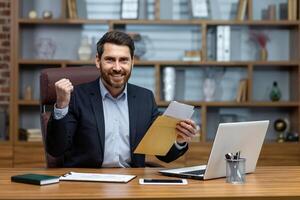 Porträt von glücklich Geschäftsmann Investor, reifen Erwachsene Mann lächelnd und suchen beim Kamera, Boss halten Botschaft Briefumschlag mit gut gewinnen Nachrichten Innerhalb Büro beim Arbeitsplatz. foto