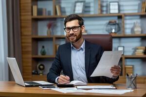 Porträt von reifen Geschäftsmann Innerhalb Büro beim Arbeitsplatz, Mann mit Unterlagen lächelnd und suchen beim Kamera, Papierkram von reifen erfahren Boss beim Schreibtisch. foto