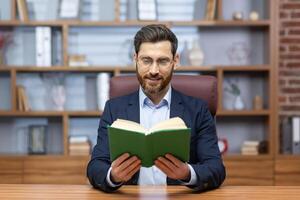 Porträt von ein jung Geschäftsmann lesen ein Buch im das Büro. das Lehrer unterrichtet Studenten dissonant durch ein Forderung, gibt ein Vorlesung. ein Pastor, ein Priester liest ein Predigt von das Bibel online. foto