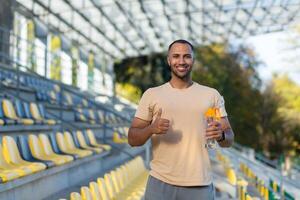 Porträt von Sportler mit Flasche von Wasser, Mann ruhen Gehen Stadion zum Ausbildung, jung Athlet Yoga und Fitness Trainer. foto