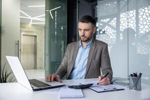 ein Fachmann männlich im ein Clever passen funktioniert aufmerksam beim seine Laptop im ein gut beleuchtet zeitgenössisch Büro Raum, zeigen Widmung und Produktivität. foto