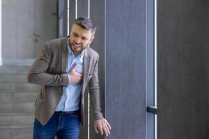 Geschäftsmann im Not umklammern Truhe durch Büro Tür, abbilden Herz Attacke, Gesundheit Krise, oder heftig Stress im korporativ Umfeld. foto