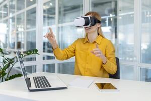 Geschäftsfrau erkunden virtuell Wirklichkeit mit vr Headset während Sitzung beim ihr Schreibtisch im ein zeitgenössisch Büro Raum. foto