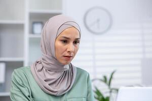 konzentriert Muslim Frau tragen ein Hijab erleben Besorgnis, Sorge oder Stress während Arbeiten im ein modern Büro Einstellung. foto