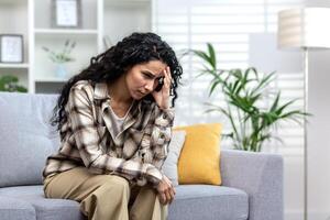 einsam spanisch Frau Sitzung allein auf Sofa im Leben Zimmer beim heim, deprimiert Frau Denken Über schwierig Entscheidung. foto