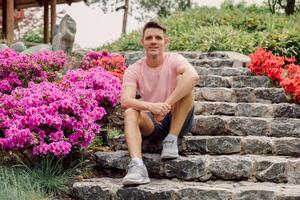 gut aussehend lächelnd Mann sitzen auf das Treppe im Sommer- Garten. foto