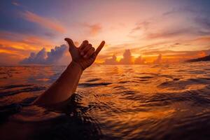Shaka Symbol mit hell Sonnenuntergang im Ozean. Lebensstil Surfen Konzept foto