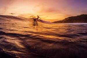 Dezember 14, 2022. Bali, Indonesien. Mann während Surfen mit Sonnenuntergang Töne. Profi Surfer Reiten auf Welle und machen Tricks. foto