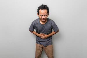 ein asiatisch Mann im grau haben Bauch schmerzen isoliert auf Weiß Hintergrund foto