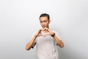 ein asiatisch Mann im ein beiläufig T-Shirt ist Herstellung ein Liebe Hand Geste foto