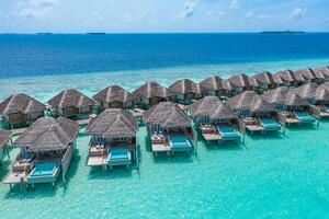 luftaufnahme der malediveninsel, des luxuriösen wasservillenresorts und des holzstegs. schöner himmel und ozeanlagune strandhintergrund. Sommerferien Urlaub und Reisekonzept. paradies luftlandschaft pano foto