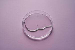 Serum oder kosmetisch Öl fließt in ein transparent Schüssel auf ein lila Hintergrund. foto