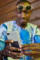 afrikanisch amerikanisch Teenager im traditionell Sudanesen Kleidung beschäftigt, verlobt mit Smartphone foto