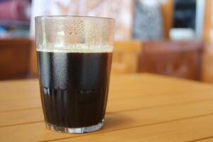Glas Tasse gefüllt mit schwarz Kaffee auf ein braun Tabelle foto