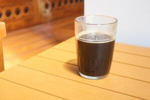 Glas Tasse gefüllt mit schwarz Kaffee auf ein braun Tabelle foto