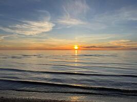Orange Sonnenuntergang Himmel mit Wolken gegen das Hintergrund von Ozean Wellen und das Küste. inspirierend Ruhe Meer mit Sonnenaufgang Himmel. bunt Horizont über das Wasser. foto