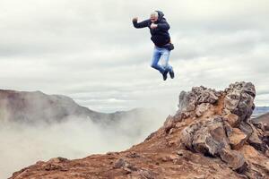 Reisender Mann Springen Über das Rauch von ein geothermisch Quelle von ein Vulkan im Island foto