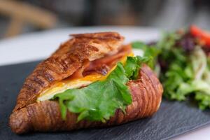 4k Frühstück Szene. ein Frau ist Essen ein Croissant mit Speck und durcheinander Eier beim Frühstück. foto