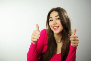 aufrichtig Lachen schön Weiß Zähne lange Haar wahnsinnig schön Mädchen wirbt etwas auf Weiß Hintergrund, sie wendet sich und Punkte zu das Seite mit ihr Finger, dann zeigt an ihr Daumen in das Rahmen foto