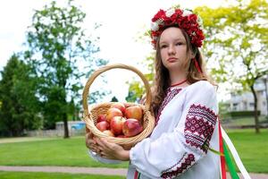 jung schön Mädchen im rot Kranz von Blumen auf ihr Kopf rot Mohnblumen im vyshyvanka rot Äpfel nehmen ein Apfel mit Hände einatmen Geruch gut Wetter im Garten zum Welt schön Mädchen Frauen von das Welt foto