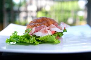 Croissant Sandwich mit Fleisch Jamon Prosciutto mit Tomate Grüner Salat Essen Reich Stücke von Käse im Frühstück Frankreich auf ein Weiß Teller teuer Restaurant Hotel bekommen ein Stück von Fleisch mit ein Gabel foto