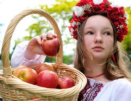 jung schön Mädchen im rot Kranz von Blumen auf ihr Kopf rot Mohnblumen im vyshyvanka rot Äpfel nehmen ein Apfel mit Hände einatmen Geruch gut Wetter im Garten zum Welt schön Mädchen Frauen von das Welt foto