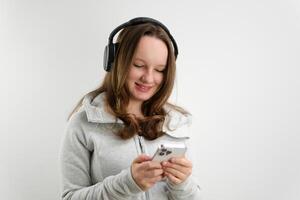 Mädchen mit Kopfhörer und ein Handy, Mobiltelefon Telefon beim ein Foto schießen Studio Weiß Hintergrund behalten ein Finger auf das Kopfhörer machen Augen Pose Mobilität Musik- Hör mal zu Spur Sportbekleidung abspielen Sport